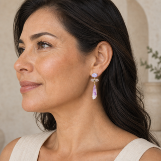 Model wearing gold tiered drop earrings with oval iridescent studs, clear crystal bars and pink elongated pendants.