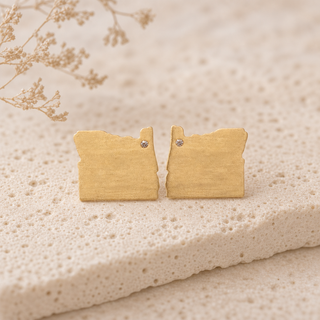 Gold Oregon-shaped stud earrings with small crystal accents.