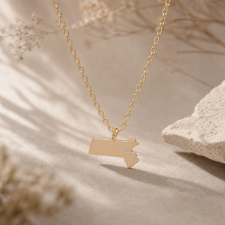 Gold chain necklace with a Massachusetts-shaped pendant and a small crystal accent.