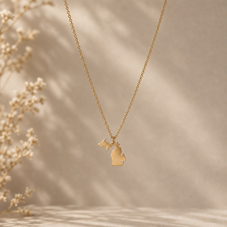 Gold chain necklace with a Michigan state pendant and a small crystal accent.