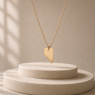 Gold chain necklace with a Nevada-shaped pendant and a small crystal accent.