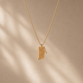 Gold chain necklace with a Rhode Island-shaped pendant and a small crystal accent.