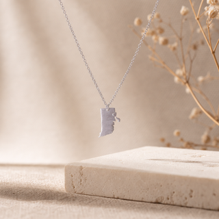 Silver chain necklace with a Rhode Island-shaped pendant and a small crystal accent.
