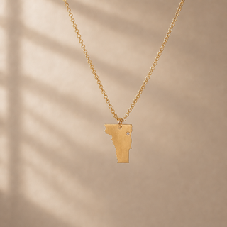 Gold chain necklace with a Vermont state pendant and a small crystal accent.