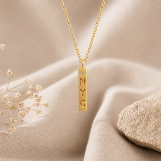 Gold chain necklace with a vertical NYC bar pendant and a small crystal accent.