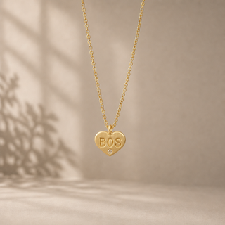 Gold chain necklace with a heart pendant stamped BOS and a small crystal accent.