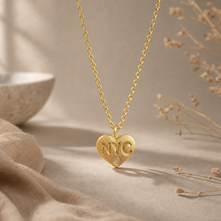 Gold chain necklace with a heart pendant stamped NYC and a small crystal accent.