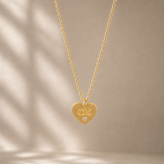 Gold chain necklace with a heart-shaped pendant stamped OK and a small crystal accent.