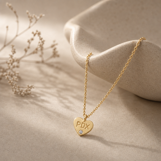 Gold chain necklace with a heart pendant stamped PDX and a small crystal accent.