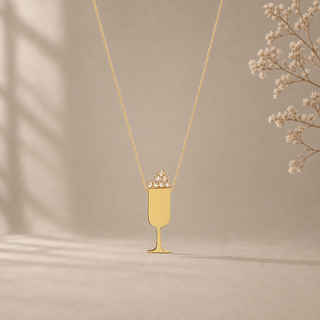Gold chain necklace with a champagne flute pendant topped with crystal bubbles.