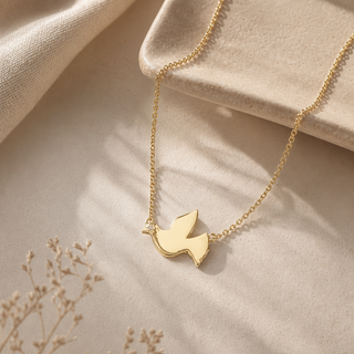 Gold chain necklace with a flying dove pendant and small crystal accents.