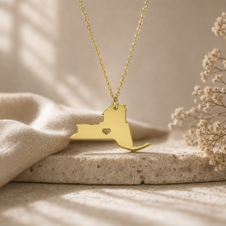 Gold chain necklace with a New York state pendant and a heart cutout.