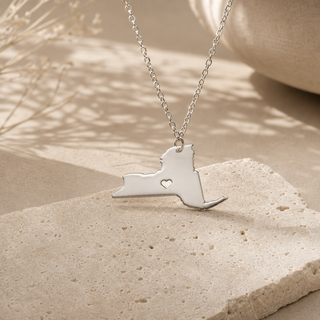 Silver chain necklace with a New York state pendant and a heart cutout.