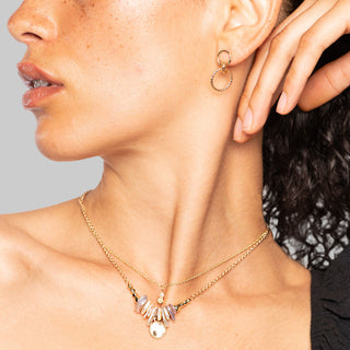 Close-up of a woman wearing gold double hoop earrings and a necklace with a gray background
