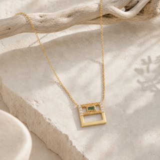 Gold chain necklace with an open square pendant, green rectangular stone and clear crystal accents.