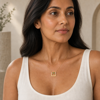 Model wearing gold chain necklace with an open square pendant, green rectangular stone and clear crystal accents.