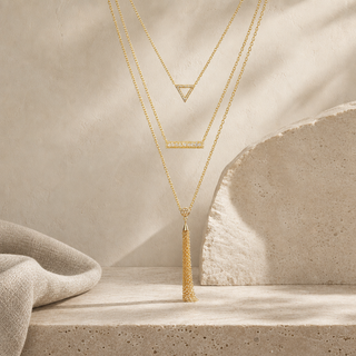 Three-layer gold necklace with an open triangle, crystal bar and long chain tassel pendants.