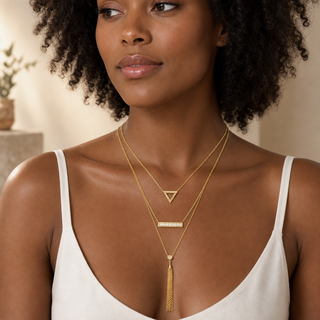 Model wearing three-layer gold necklace with an open triangle, crystal bar and long chain tassel pendants.